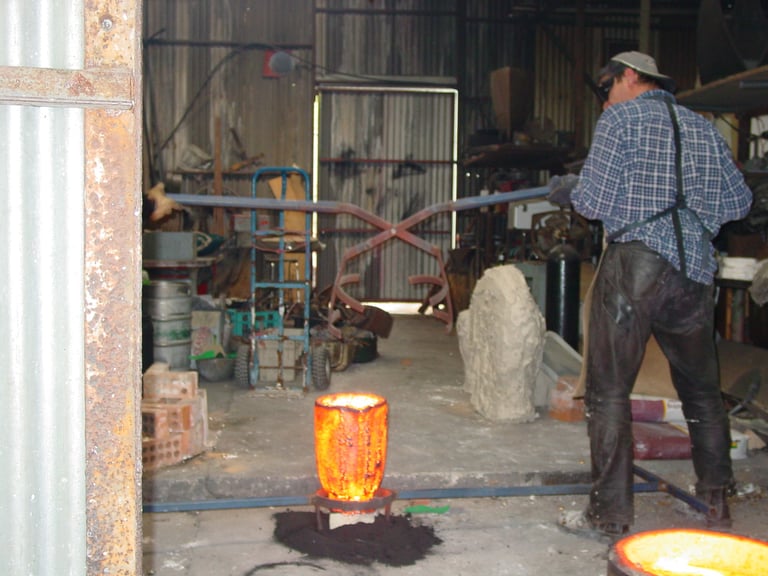 Positioning the tongs to lift the crucible of bronze for pouring