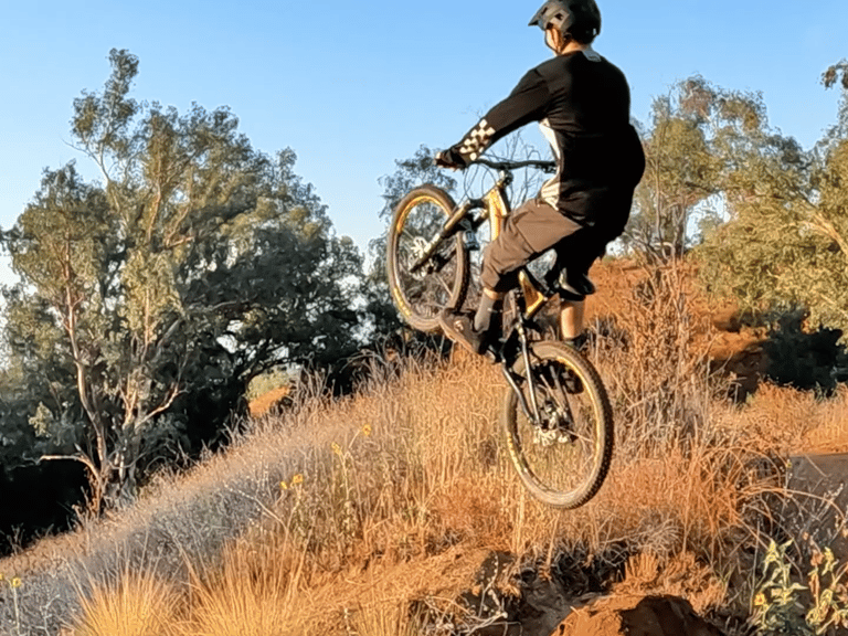 Mountain biker leaning too far back mid-air, about to land rear wheel first on a dirt jump — risk of