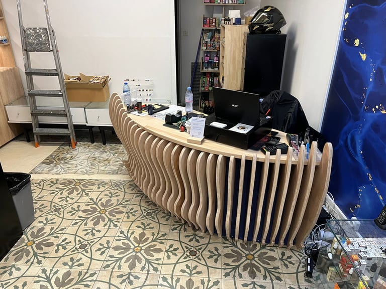 Modern curved wooden slat reception desk in a shop with patterned floor tiles and shelving.