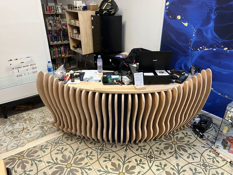 Modern curved wooden reception desk with vertical slats in a shop with patterned floor tiles.