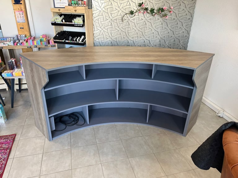 Curved wood and grey reception desk with open shelving for a retail store or boutique checkout.