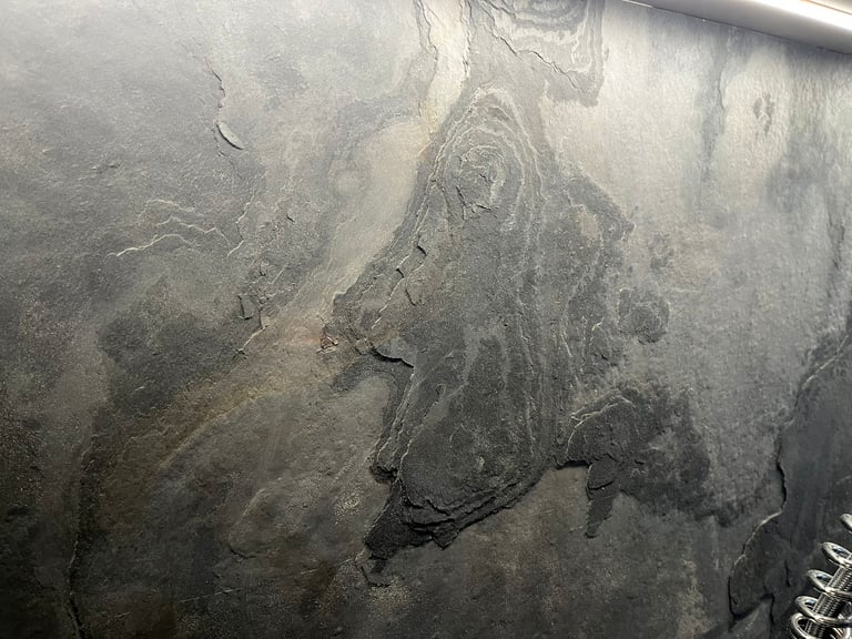 Close-up of a natural grey slate stone wall with textured layers and rustic mineral patterns.