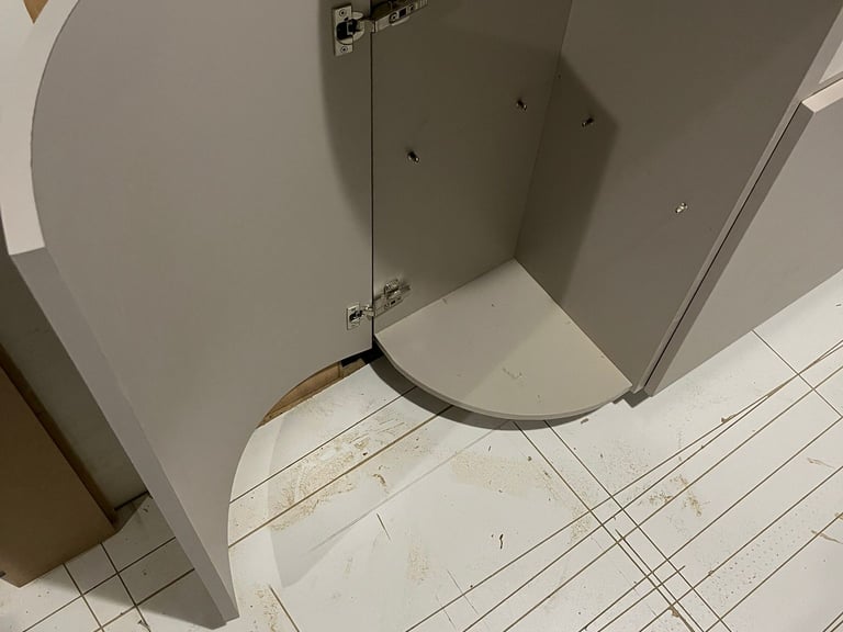 Modern curved light grey kitchen cabinet with an open door showing interior hinges and stone countertop.