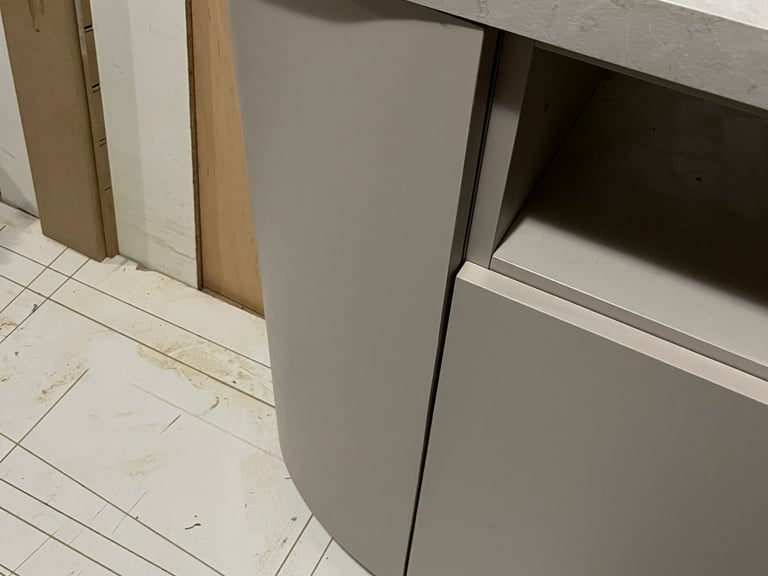 Modern curved light grey kitchen cabinet with a stone countertop during installation.