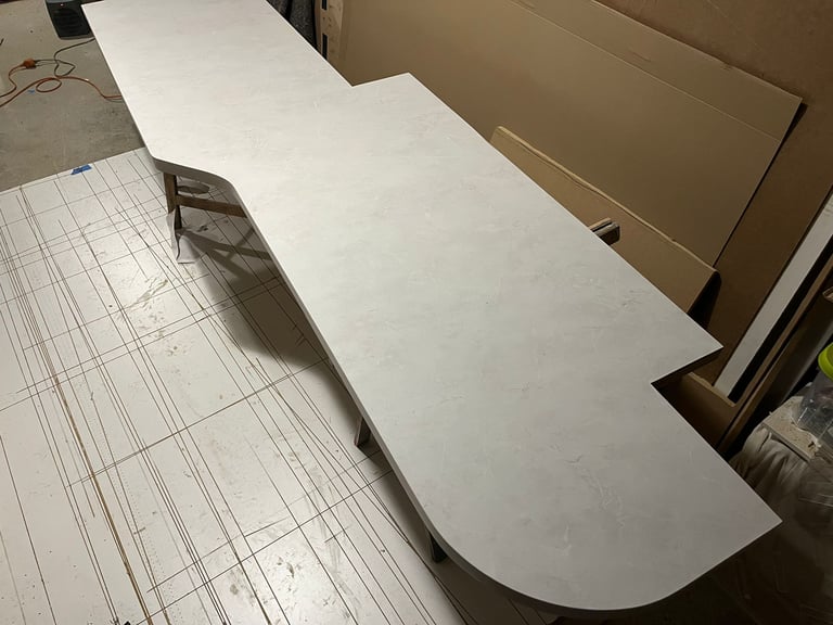 Custom white marble laminate countertop with a curved edge being fabricated in a workshop.