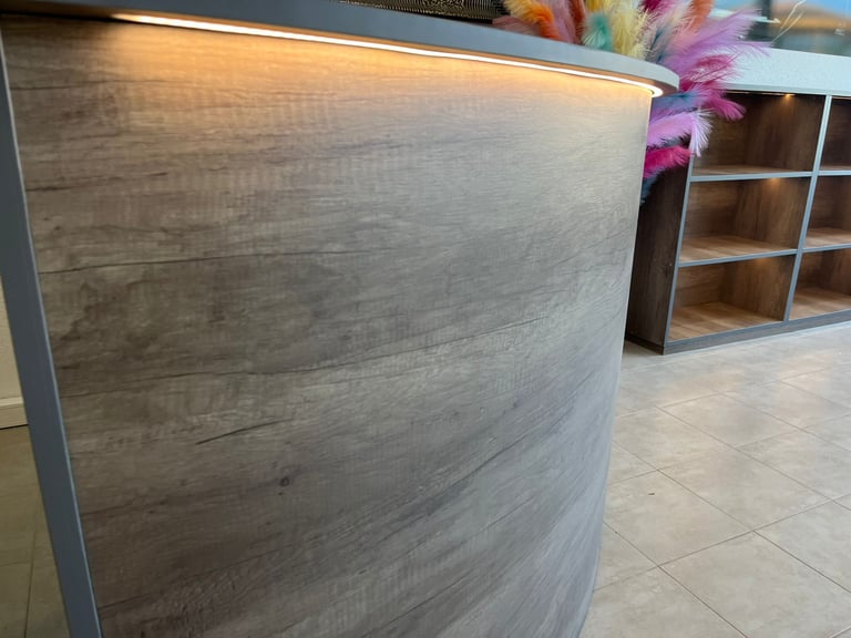 Curved wood reception desk with LED strip lighting in a modern commercial office interior.