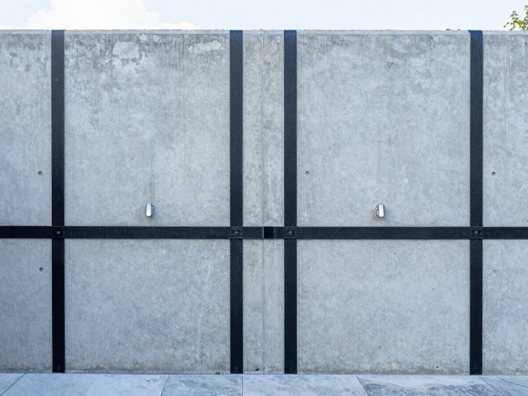 Straight-on architectural photograph of a clean concrete basement wall with neat carbon fiber reinforcement straps installed vertically, bright utility lighting, cool slate tones, 35mm.