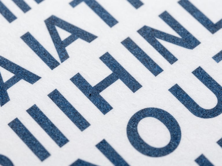 Close-up macro shot of structured typographic layout on thick white cardstock, slate ink, clean geometric grid lines, flat lighting