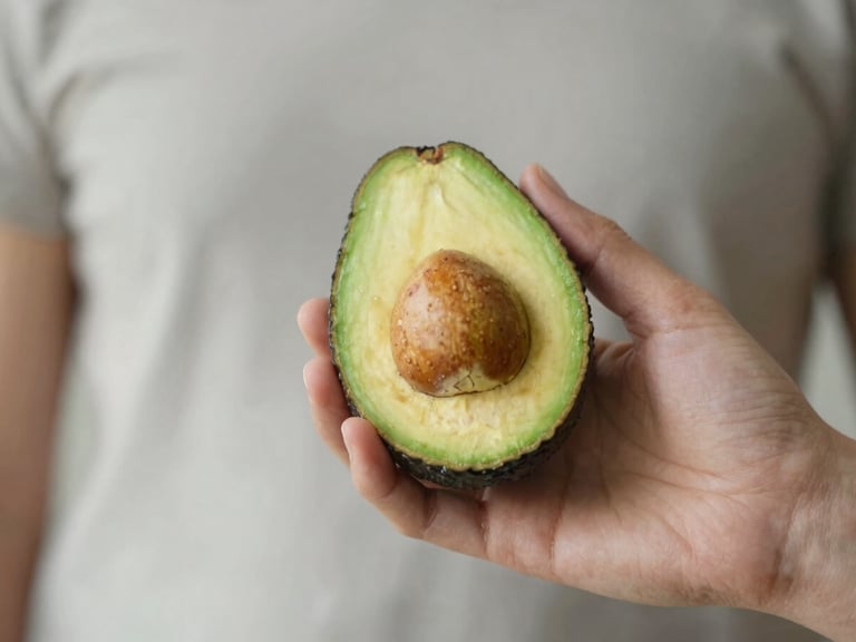 Close-up of a human hand holding a ripe avocado, soft natural light, shallow depth of field, muted organic tones.