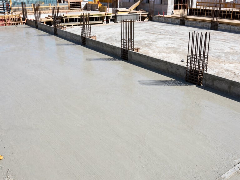Wide-angle shot of a construction site with fresh concrete being poured into forms, rebar visible, bright natural daylight, clean realistic tones.