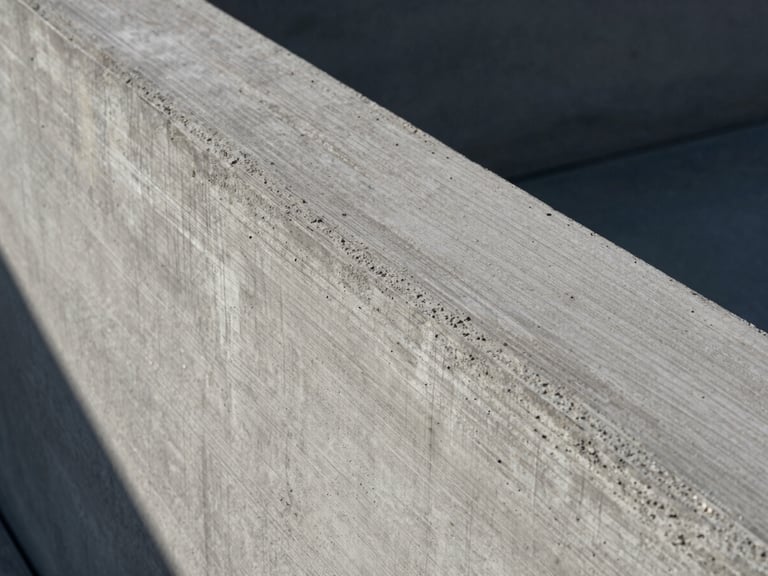 Extreme close-up of cured architectural concrete showing wood-grain formwork texture under harsh midday sun casting deep shadows.