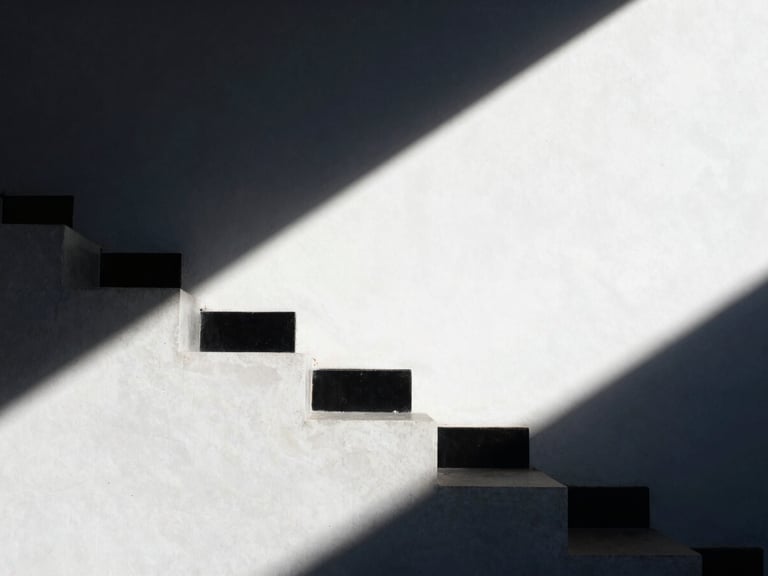 An abstract close-up of a minimalist concrete staircase casting sharp diagonal shadows, clean architectural lines, high-contrast natural light, deep navy shadows and bright white surfaces.