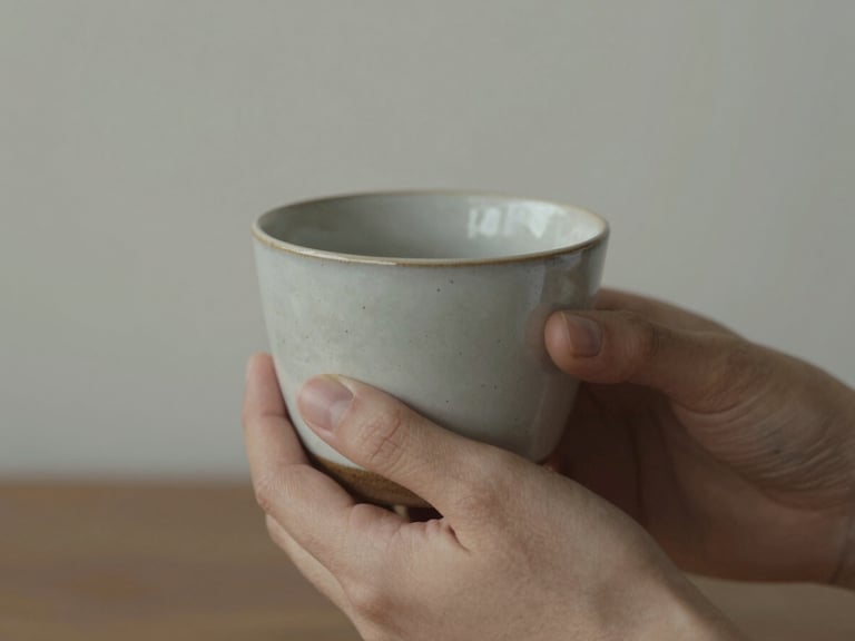 A close-up of a person's hands holding a warm ceramic cup, soft overcast light, muted earth and sage tones, shallow depth of field, 35mm