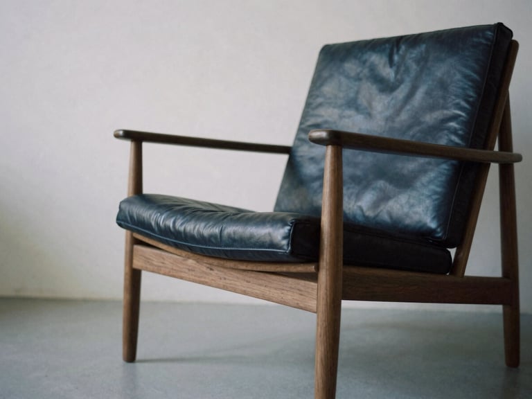 Architectural furniture photography, low-angle shot of a minimalist lounge chair in American walnut and full-grain leather, soft side daylight, deep navy shadows.