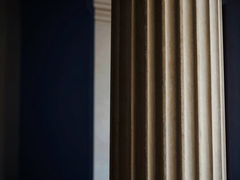 Architectural detail of a classical fluted column, illuminated by soft, dramatic window light, shallow depth of field, deep navy and warm brass tones.