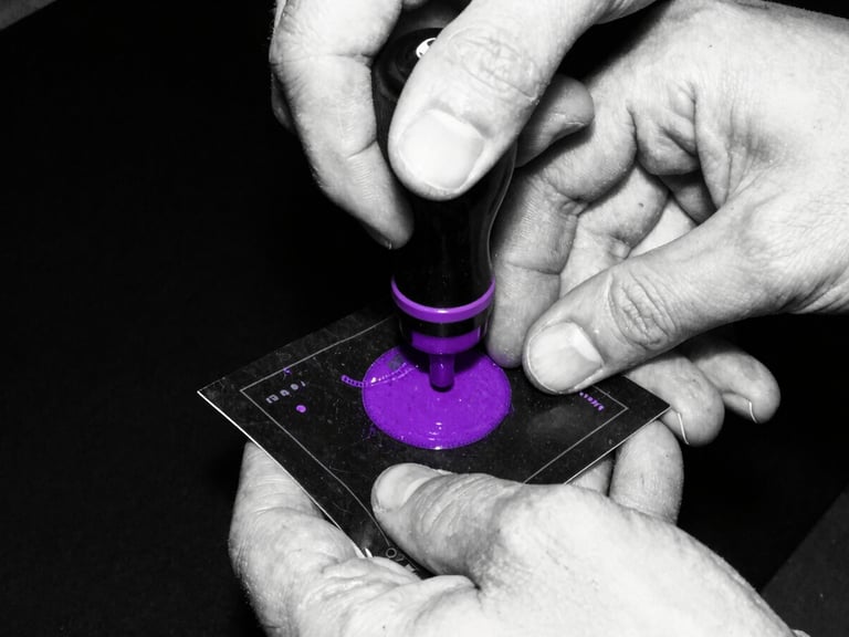Close-up of hands stamping a dark ticket with purple ink, high-contrast black and white