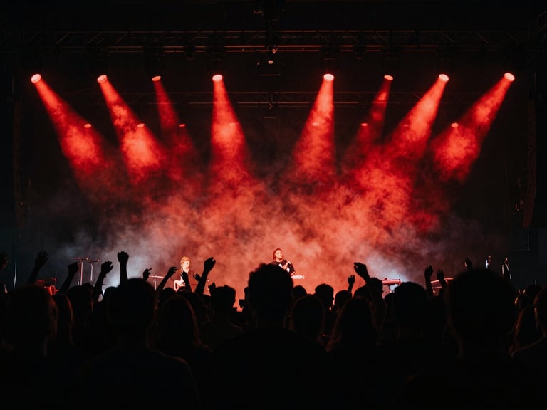 Dynamic shot of a concert crowd with dramatic stage lighting, smoke, and vibrant red spotlights, captured from behind the sound engineer, cinematic film photography, high contrast, deep blacks.