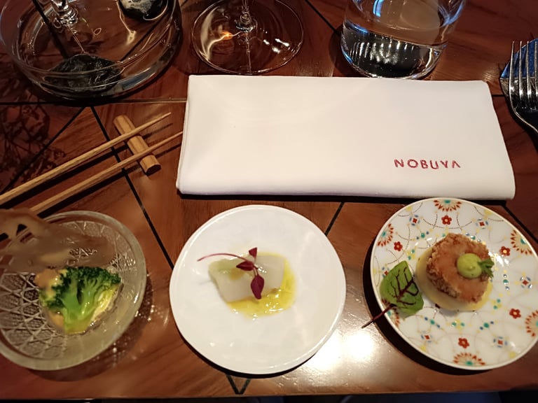 Piccoli assaggi serviti al tavolo del ristorante Nobuya Milano con tovagliolo ricamato Nobuya e mise en place