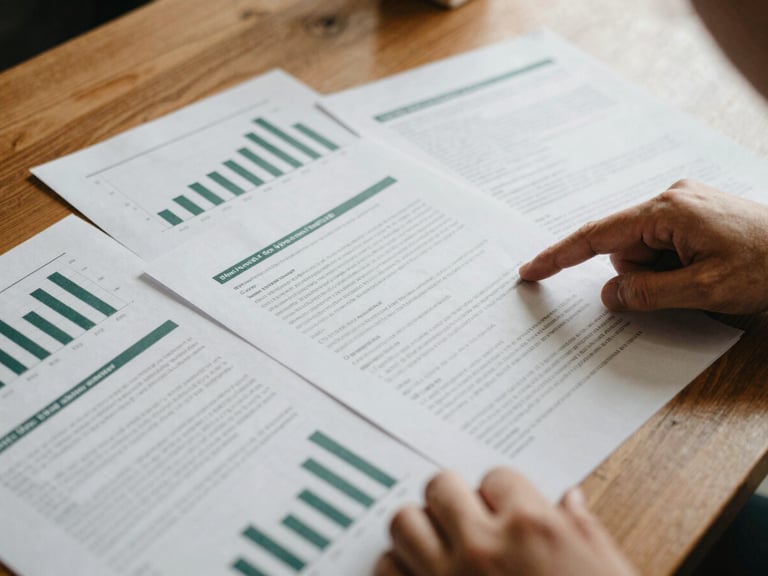 Close-up of printed policy briefs and statistical charts on a wooden table, warm indoor ambient light, hands pointing at data, selective focus