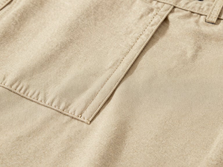 Macro close-up of premium warm beige chino fabric texture, sharp focus on clean stitching and weave, soft diffused daylight, 35mm lens
