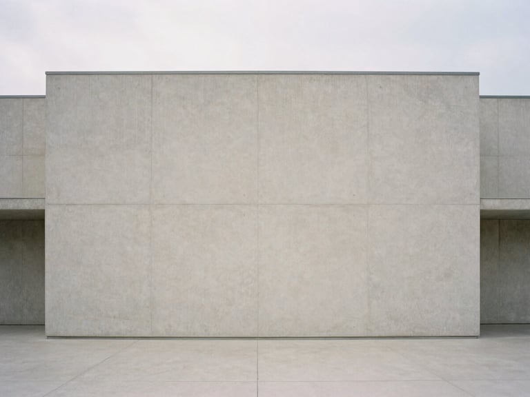 Straight-on architectural shot of minimalist concrete building facade under soft overcast daylight, clean geometric lines, vast negative space, muted tones, quiet atmosphere.