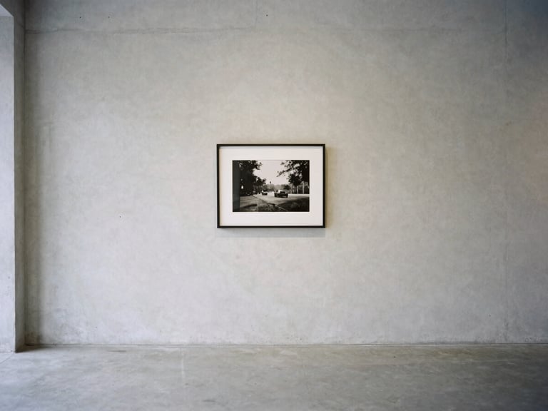 A quiet minimalist gallery space with soft natural light, empty concrete walls, single framed black and white photography on the wall, medium format film, clean composition