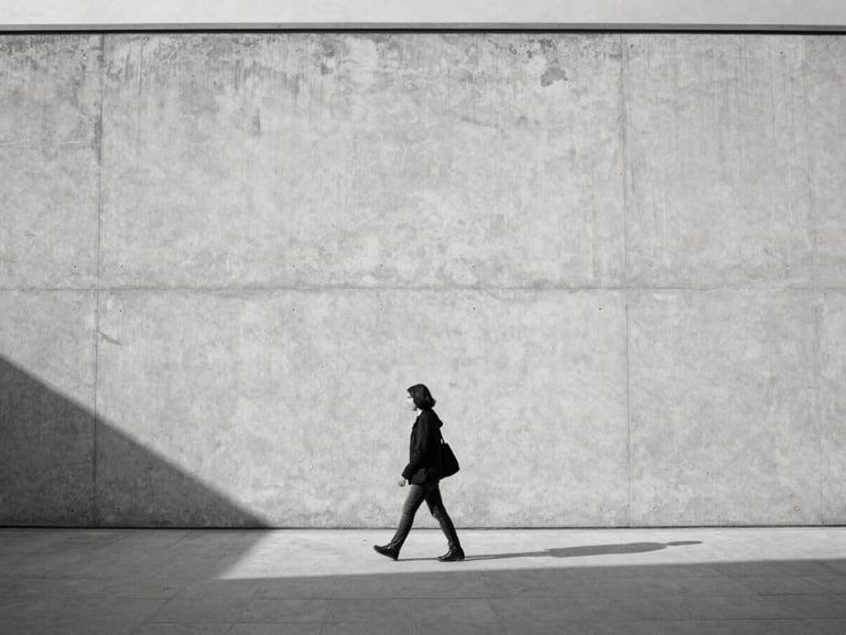 A lone figure walking past a massive minimalist concrete wall in Ankara, sharp shadows, soft natural light, medium format black and white photography.