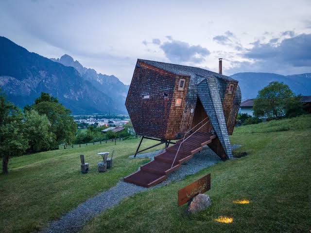 Modern wooden mountain cabin with a unique geometric design overlooking the Austrian Alps at dusk.