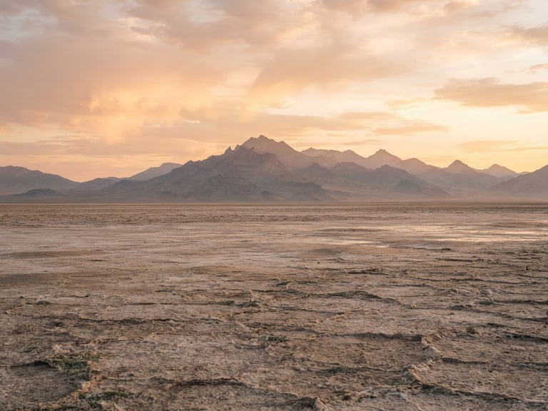 Sweeping natural vista of Utah's salt flats and distant mountain ranges at golden hour, soft diffused light, wide environmental shot, warm editorial photography.