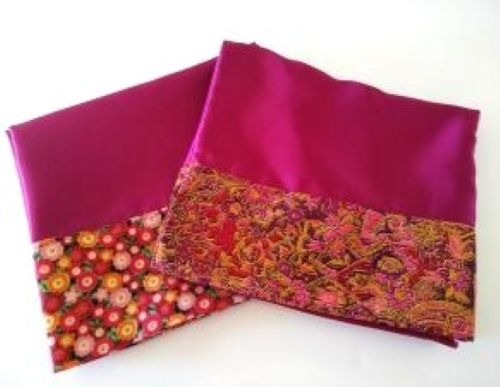 Two burgundy satin pillowcases hemmed with floral trim on a white background.