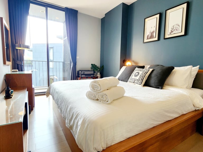 Modern hotel bedroom with a king-size bed, white linens, and blue accent wall near a private balcony.