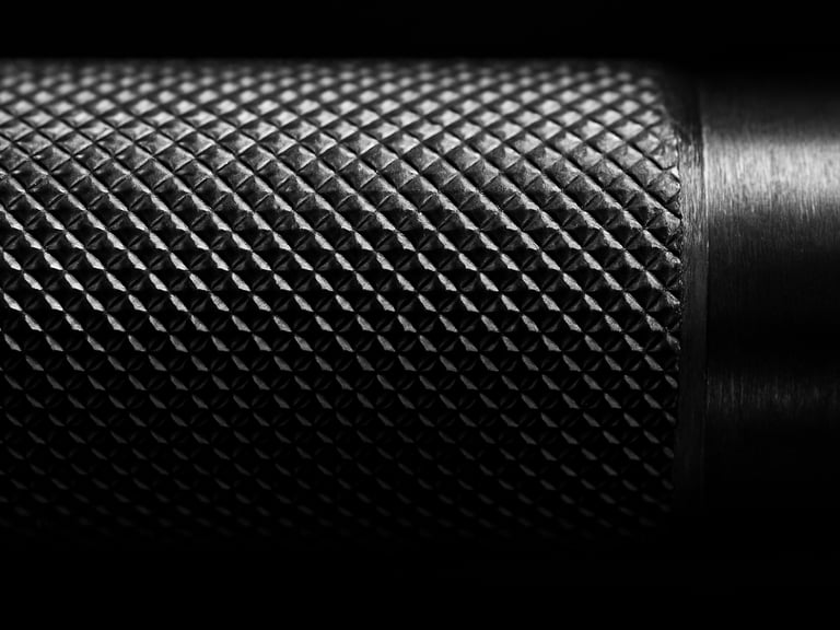 Extreme macro shot of precise knurling on a chrome barbell shaft, dramatic side lighting carving the metallic textures, sharp focus, 50mm.
