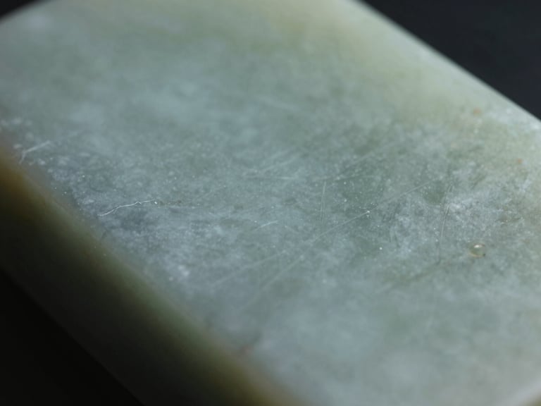 Close-up of smooth jade-toned stone surface, cool diffused studio light, fine grain and mineral variation visible, quiet empty composition
