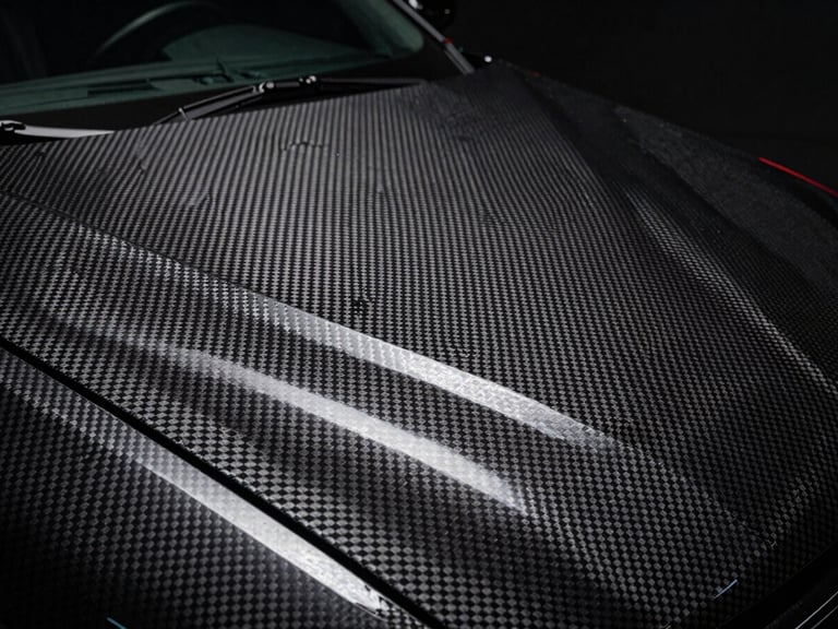 Macro shot of a carbon fiber texture vinyl wrap on a car hood, dramatic studio lighting, 50mm