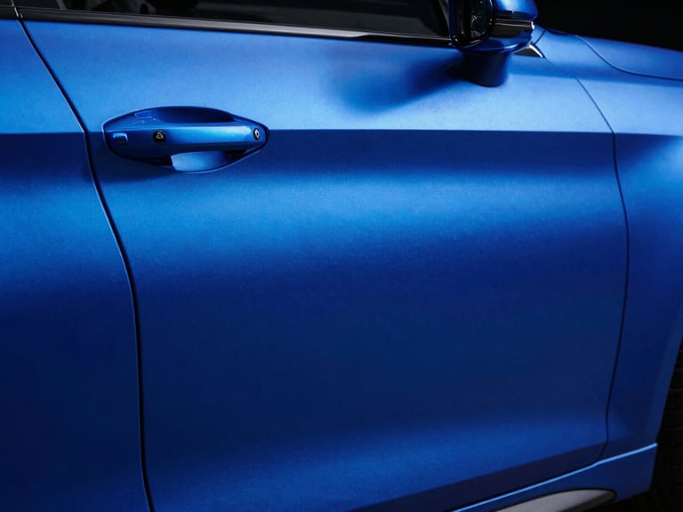Close-up of a matte metallic blue liquid-wrapped car panel, studio lighting, deep shadows, 50mm