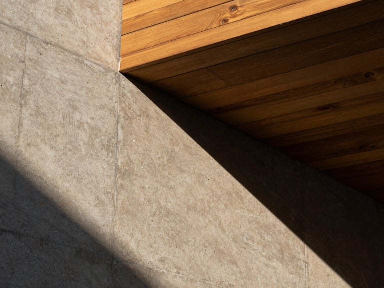Architectural close-up of raw textured concrete and warm wooden slats under the high-contrast late afternoon Paracas sun, geometric shadow patterns.