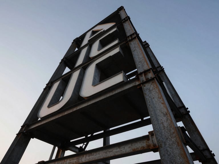 Low angle shot of a massive steel totem sign structure against a clear sky, dramatic industrial lighting, raw steel textures.
