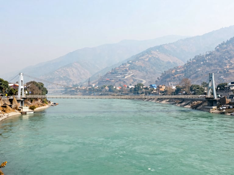 Panoramic view of Rishikesh suspension bridge over the turquoise Ganges river, misty mountains in the background, bright daylight.
