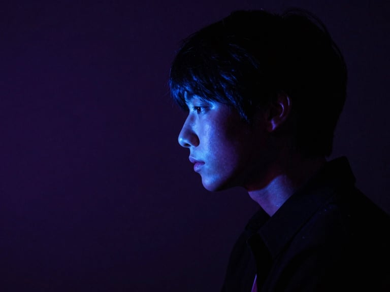 Moody atmospheric shot of a person in deep contemplation, illuminated by a single sharp neon blue light source, deep shadows, 35mm lens