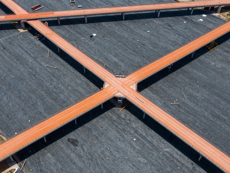 Aerial drone perspective of a structured landscape (e.g., bridge construction) in the Mid-Atlantic region, crisp daylight, high-contrast slate and orange tones, sharp focus, architectural lens.