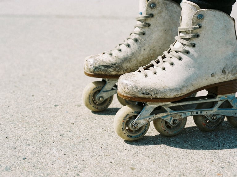 Close-up of vintage inline skates from the 90s, worn wheels, grind plates, on raw concrete, harsh direct sunlight, gritty film photography.