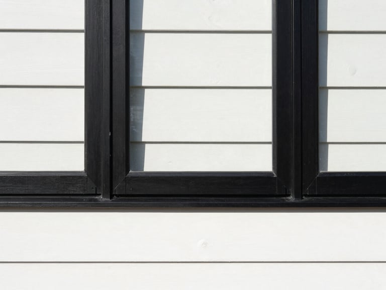 Straight-on architectural detail of a newly installed black window frame against clean white siding, crisp paint line, direct daylight.