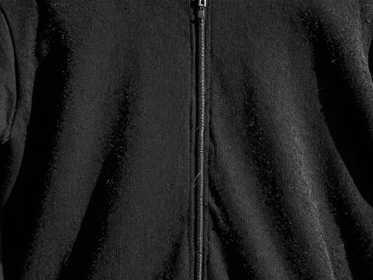 Dettaglio macro di una cucitura rinforzata su un capo di abbigliamento nero, con fili spessi e un leggero effetto distressed, luce dura e ombre nette.