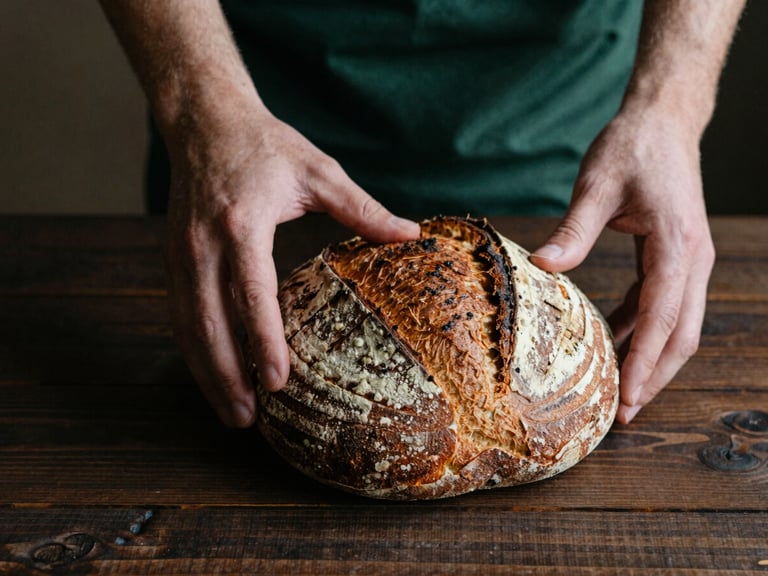 Hands arranging rustic sourdough bread on a dark wooden table, soft natural side-light, moody Scandinavian style, rich tones, 35mm