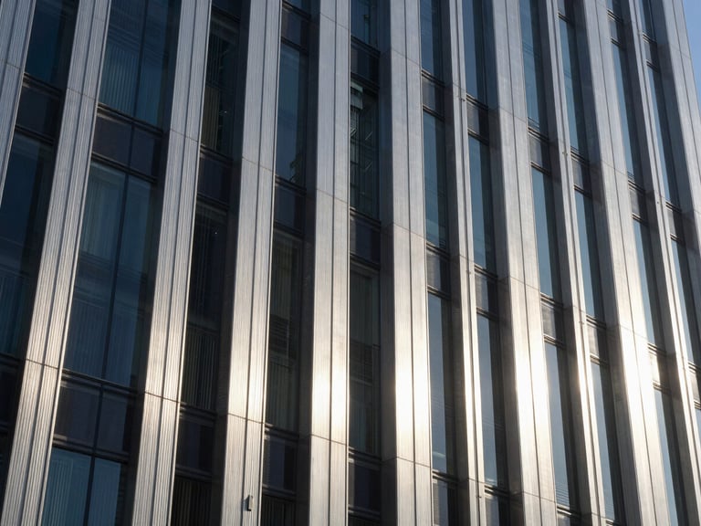 Crisp daylight architectural detail of a modern financial district skyscraper, brushed steel and glass facade, deep shadows, cool silver tones.