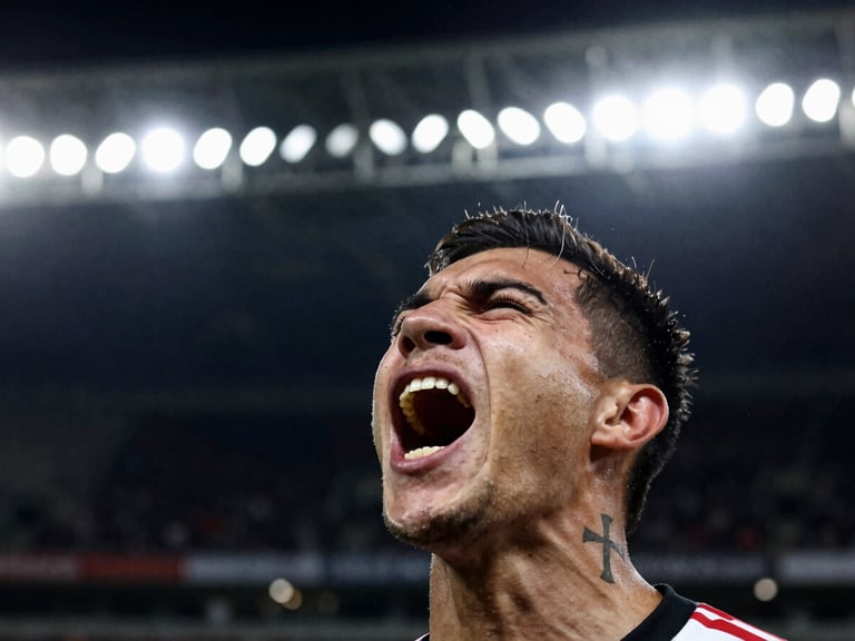 Close-up of a passionate fan screaming with joy, Maltese cross tattoo visible on shoulder, high contrast stadium floodlights, 35mm