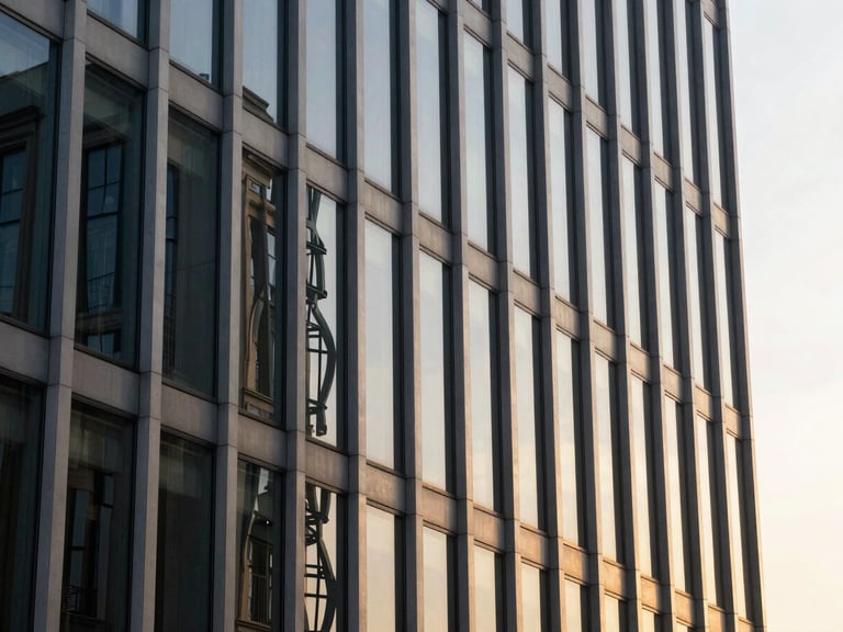 Architectural detail of a glass and steel corporate facade reflecting warm sunset light, sharp lines, editorial composition.