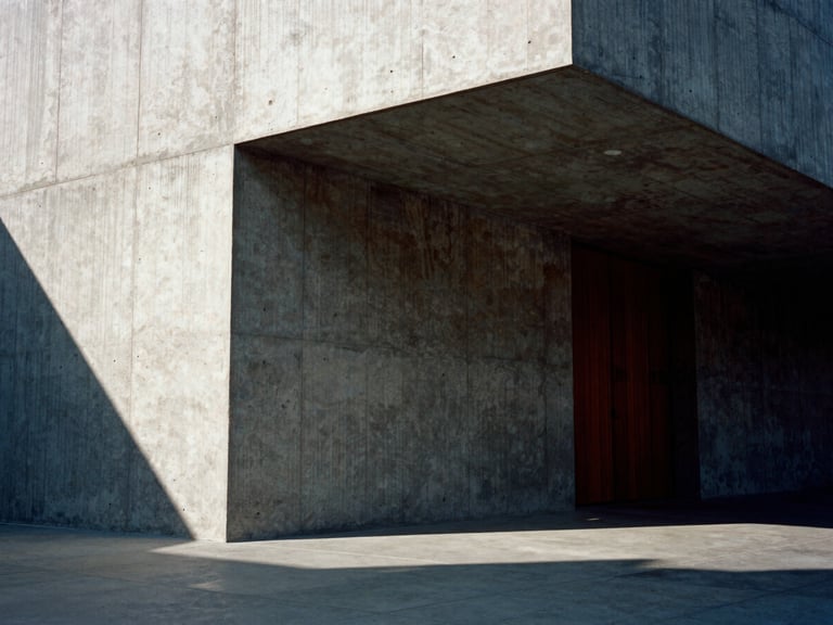 Dramatic eye-level shot of a monolithic concrete architectural model, harsh afternoon side-lighting casting deep shadows, raw concrete texture, 35mm film