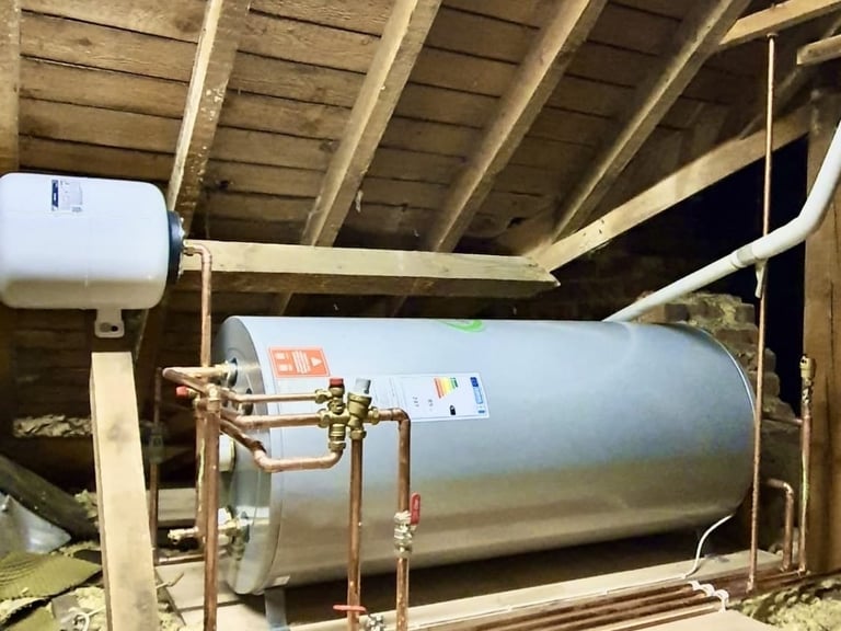 A horizontal unvented hot water cylinder installed in a wooden attic with copper pipework and expansion vessel.