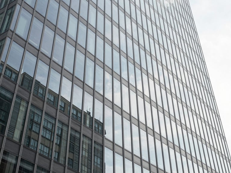 Wide-angle architectural view of a modern glass skyscraper facade reflecting clean daylight, desaturated cool tones.